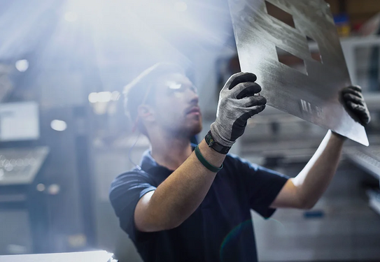 SUPER_Arbeiter A worker is examining a sheet of metal critically.