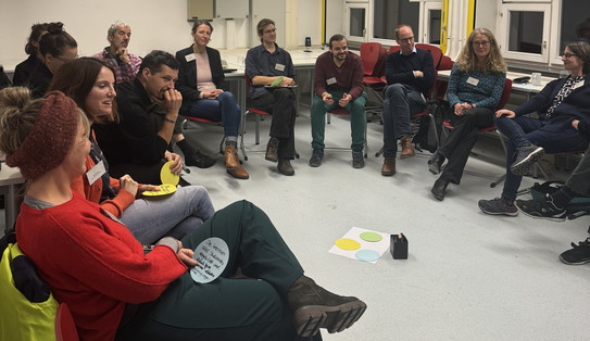 Participants sit in a circle of chairs and discuss as part of a workshop.