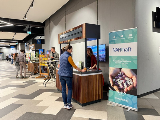 Ein Ausstellungsstand in einem modernen Innenbereich mit dem Fokus auf nachhaltige Ernährung. Im Hintergrund sind weitere Stände und Besucher zu sehen.