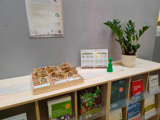 Seed library Shelf with books, plants and a box containing seeds in small bags.