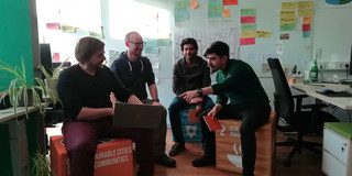 Ein Student und ein wissenschaftlicher Mitarbeiter aus der Fakultät Raumplanung sowie zwei Mitarbeiter aus dem Nachhaltigkeitsbüro sitzen auf SDG-Würfeln in einer Runde und diskutieren über die Planung einer summer school sustainability.