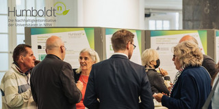Diskussionrunde vor einer Posterwand. Darüber das Logo von HumboldtN 