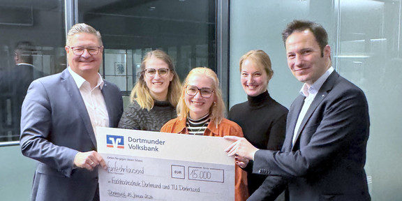 Drei Studentinnen bekommen von zwei Vorständen der Dortmunder Volksbank einen Spendenscheck überreicht.