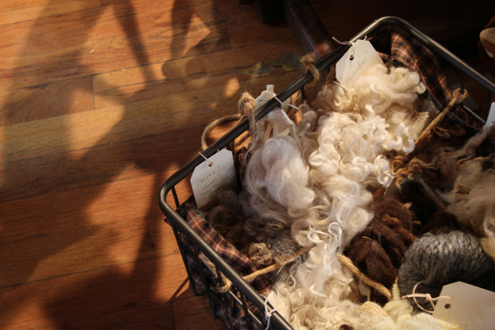 The picture shows a basket on a parquet floor. There is wool and yarn in the basket.