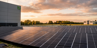 Eine große Fläche mit Solarpaneelen liegt neben einem Gebäude.