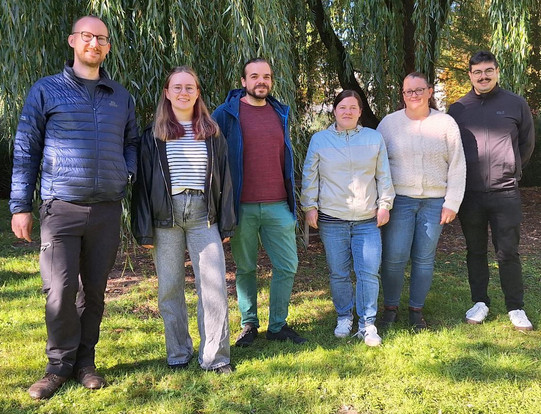 Gruppenfoto: Sechs Personen auf einer Wiese, gucken in die Kamera und lächeln.
