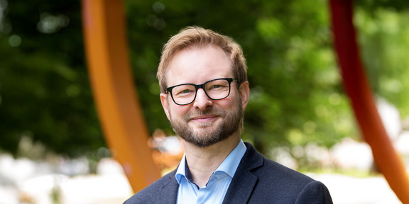 Porträtfoto von Prof. Andreas Steffen: Prof. Steffen hat blonde Haare, einen Bart und eine Brille und steht auf dem Campus der TU Dortmund.