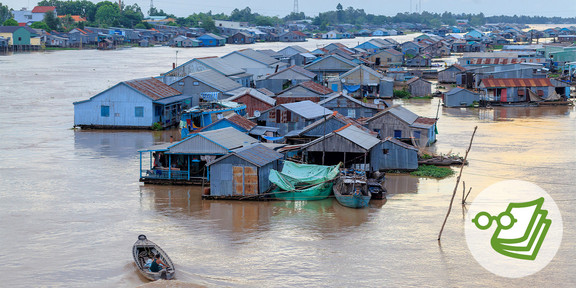 Houses are standing in the water in Vietnam and a small boat is sailing at the bottom left. 