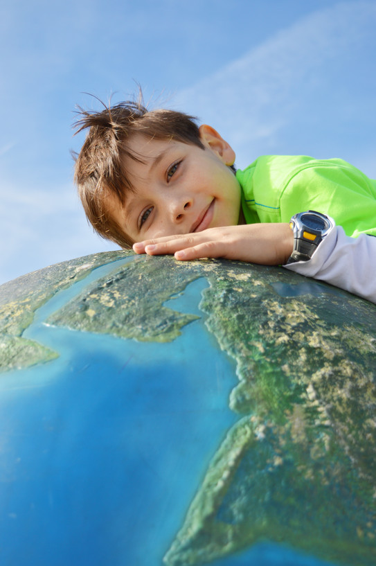 A small boy lies down with his upper body on a large globe.