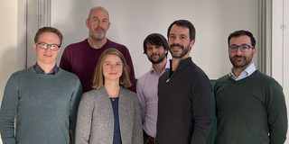 Foto: Eine Gruppe von Personen steht vor einer Präsentationsfolie mit dem Titel „GaiaIsotopic“ an der TU Dortmund, die ein technisches Gerät und Projektinformationen zeigt.