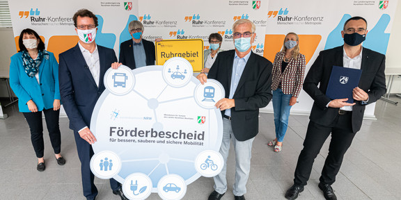 Several adults with masks can be seen. Two men hold up a poster. In the background are banners with the inscription Ruhr Conference.