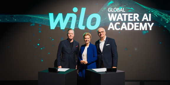 Auf dem Foto sieht man Oliver Hermes, Ina Brandes und Rektor Prof. Manfred Bayer vor einer digitalen Leinwand stehen. Sie stehen nebeneinander und lächeln für das Foto in die Kamera.