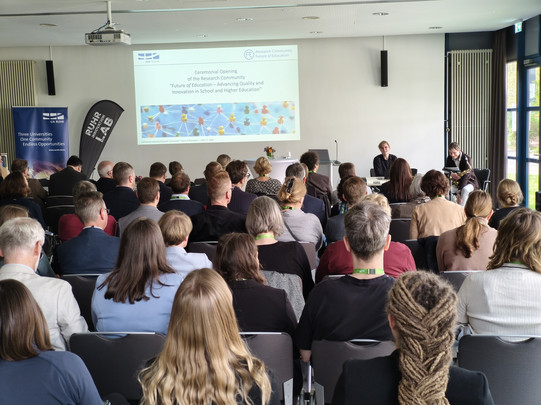 Foto: Publikum sitzt im Tagungsraum und schaut nach vorne