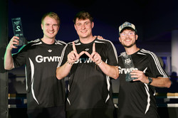 Foto: Drei Personen in schwarzen Trikots stehen zusammen, während zwei von ihnen Auszeichnungen in den Händen halten.