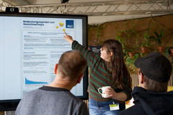 Foto: Eine Studentin erklärt Interessierten ihre Forschung anhand eines Posters.