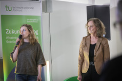 Foto: Zwei Personen sprechen vor einem Banner der Technischen Universität Dortmund.