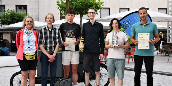 Foto: Eine Gruppe von sechs Menschen steht auf einem Platz in der Dortmunder Innenstadt. Sie halten Urkunde und Trophäen in den Händen.