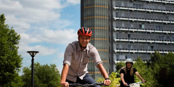 Ein Mann und eine Frau fahren vor dem Mathetower der TU Dortmund Fahrrad.