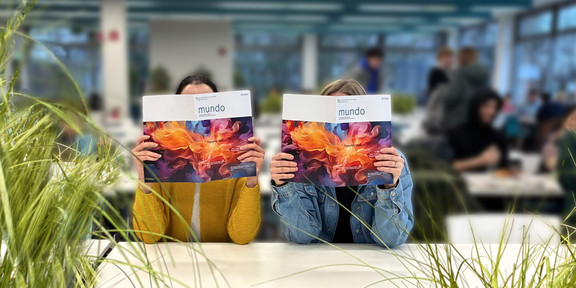 Foto: Zwei Personen sitzen an einem Tisch und zeigen die Zeitschrift „mundo“.