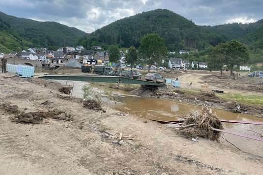 The picture shows a place destroyed by floods with broken houses and devastated landscape.