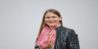 Ein Foto einer Frau mit Brille, gemustertem Oberteil und rosa Schal.