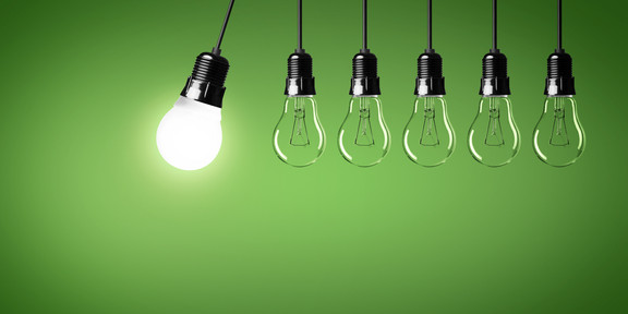 In front of a dark green background, six light bulbs hang next to each other in a row on black cables. The leftmost bulb is the only one that is lit and it swings in from the left, towards the other five bulbs.