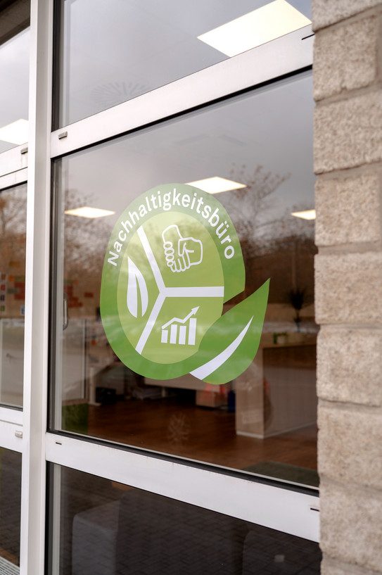 The green and white logo of the sustainability office of the TU Dortmund is stuck to a window pane.