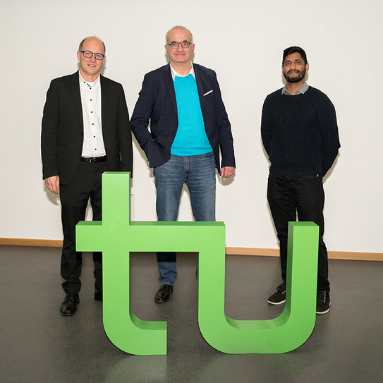 Drei Personen stehen hinter dem Logo der TU Dortmund.