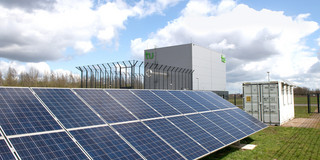 Photovoltaikanlage auf grünem Rasen mit Wolken am Himmel.