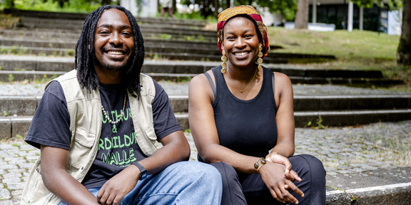 Photo: Two people are sitting on a stone staircase surrounded by greenery on campus.