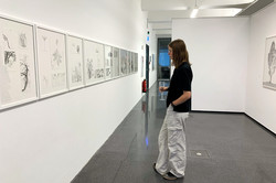 Das Bild zeigt eine Frau in einem Ausstellungsraum auf eine Wand mit Bildern blickend.