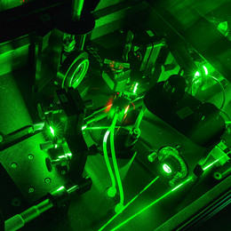 Eine Detailaufnahme eines Lasers im Labor in dunkel grünen Farben.