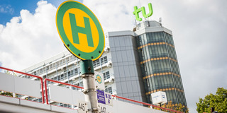 Bus stop sign with mensa bridge and maths tower in the background.