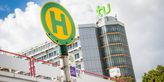Bus stop sign with mensa bridge and maths tower in the background.