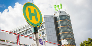 Bushaltestellenschild vor TU Dortmund Gebäude Bushaltestellenschild mit Mensabrücke und Mathetower im Hintergrund.