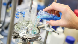 A hand fills a turquoise blue liquid into another glass vessel in the laboratory.