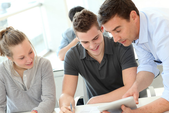 Drei Studierende stehen um einen Tisch und arbeiten gemeinsam.