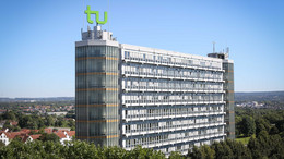 1: Mathematik Mathematikgebäude mit Mathetower: Ein hohes Gebäude mit vielen Fenstern und je einem Turm an beiden Seiten. Auf dem linken Turm ein grünes TU-Logo. Im Hintergrund Häuser und Bäume.