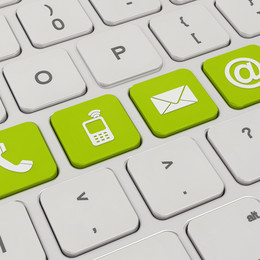 A white keyboard with four green keys. On the green keys are symbols like a telephone, a cell phone, an envelope and an „@“