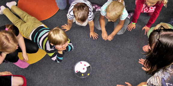 A group of children siting and lying on the floor in a circle around a can.