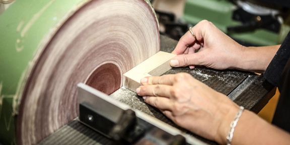 A person is grinding a piece of wood on a grinder.