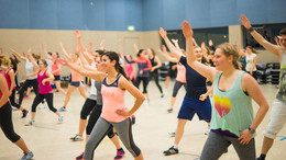 Teilnehmerinnen und Teilnehmer eines Fitness-Kurses in einer großen Sporthalle