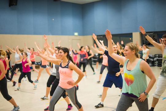 Teilnehmerinnen und Teilnehmer eines Fitness-Kurses in einer großen Sporthalle