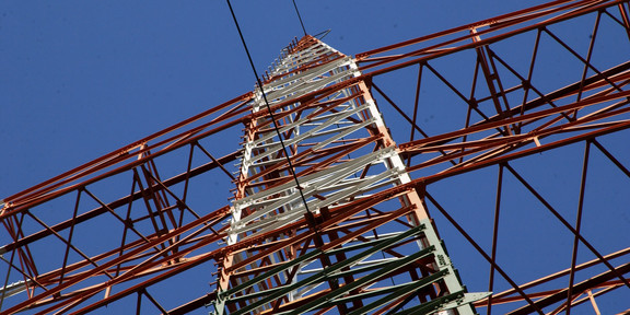 A power pole from below with blue sky in the background.