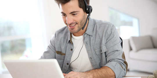 Mann sitzt vor dem Laptop und hat ein Headset auf.