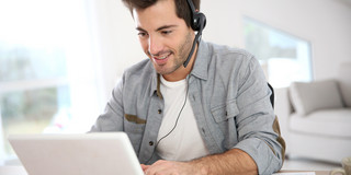 Man sits in front of the laptop and has a headset on.