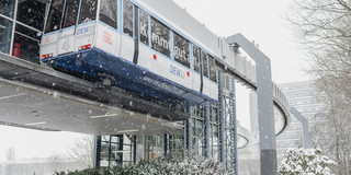 An H-train car stops at a stop on campus and snow is falling.