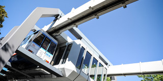 The H-Bahn is in a station and the sky in the background is blue.