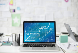 A laptop with mathematical formulas stands on a white desk next to a cup, pens and sheets of paper.