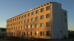 8: Elektrotechnik und Informationstechnik Gebäude E-Technik: Ein hohes weißes Gebäude, das von der Sonne angestrahlt wird. Vor dem Gebäude eine Rampe und über dem Eingang ein Vordach.